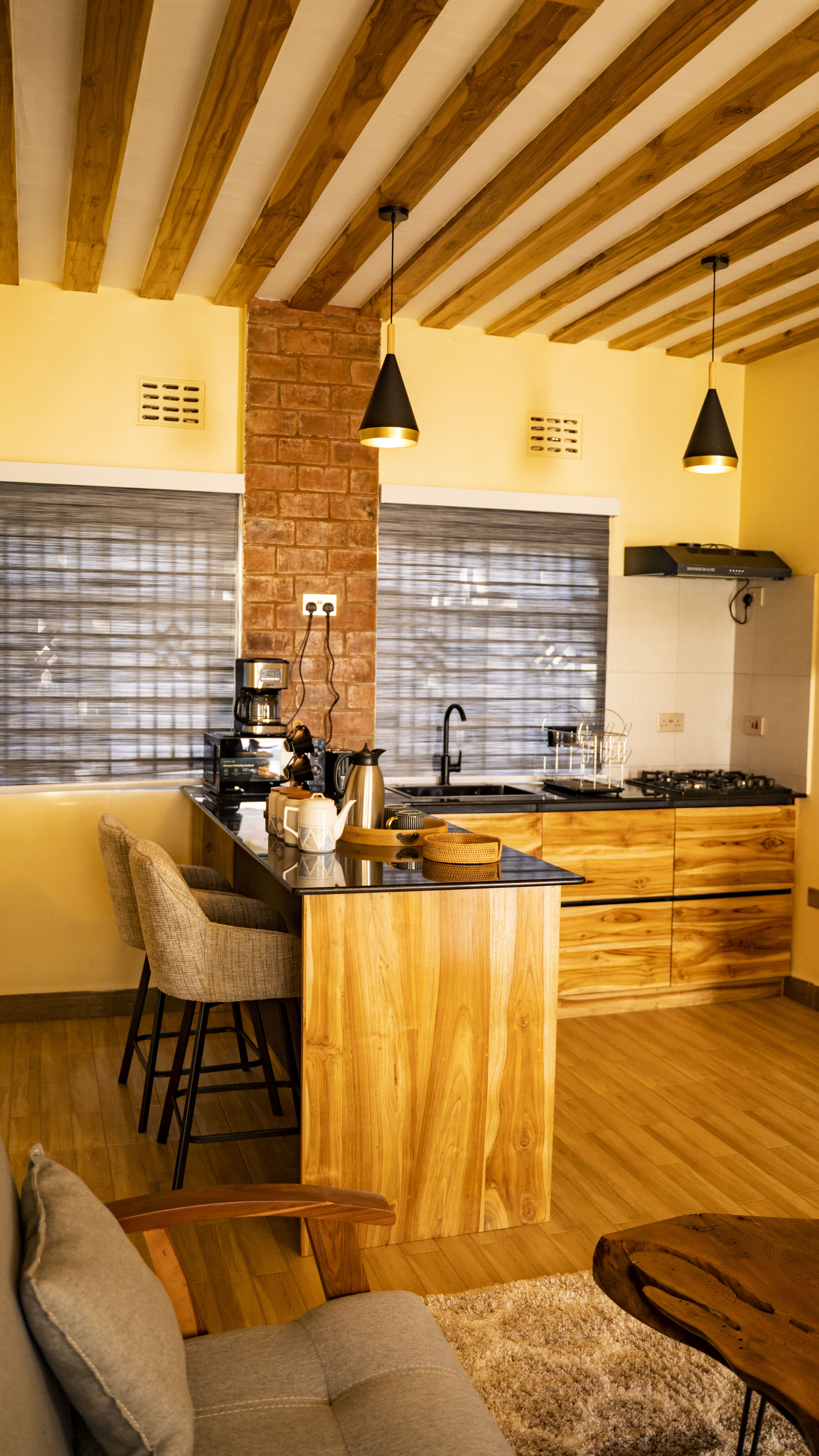 Open-plan kitchen at Lalashe Homes — handcrafted mninga cabinetry, black granite countertops and exposed timber ceiling beams