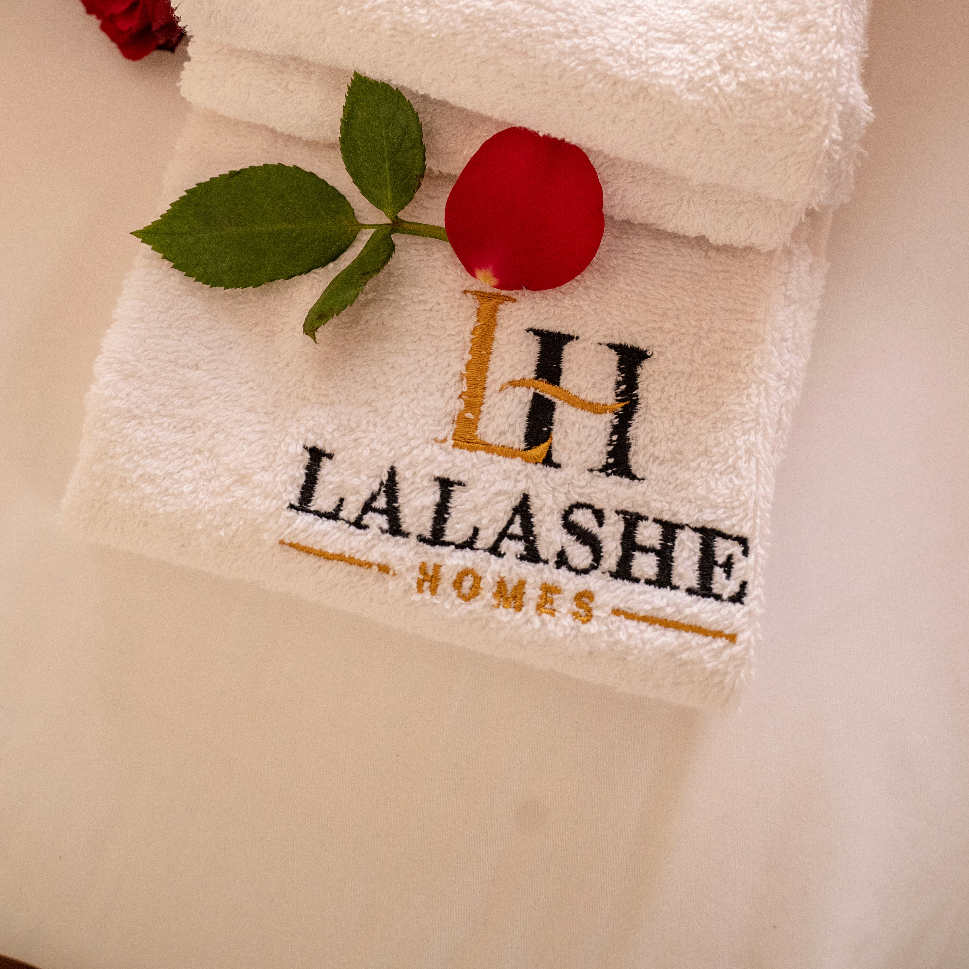 Lalashe Homes embroidered towels — the LH monogram and brand name stitched in gold and black on crisp white cotton